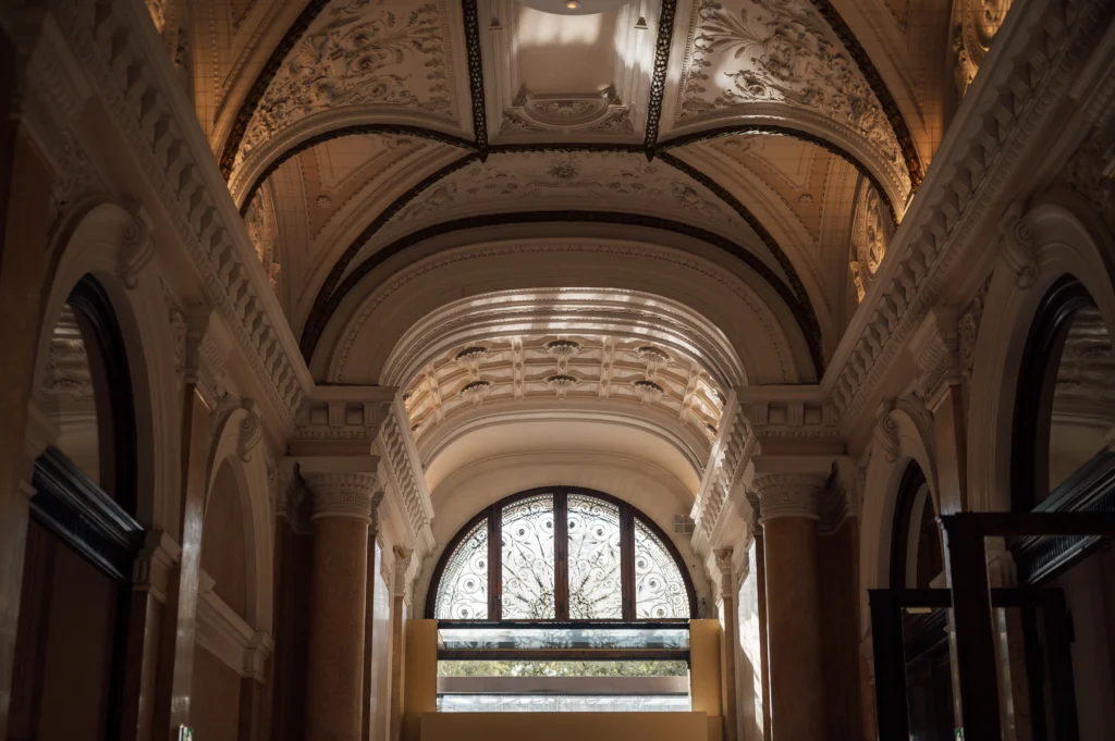 Ornate arched ceiling with decorative plasterwork and a large, patterned arched window letting in natural light.