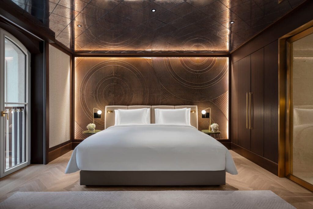 A modern hotel room with a large bed, decorative wall panelling, built-in lighting, small bedside tables with lamps, and a wardrobe on the right—an ideal space for relaxing after a long day of Data Analytics or Marketing Consultancy work.
