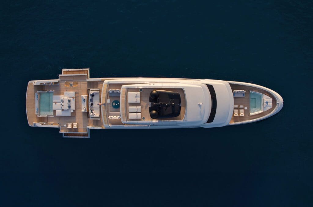 Aerial view of a large luxury yacht with multiple decks, pools, and lounge areas, floating on calm dark blue water.