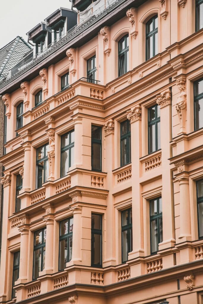 A peach-coloured historic building with decorative mouldings, large windows, and classical architectural details.