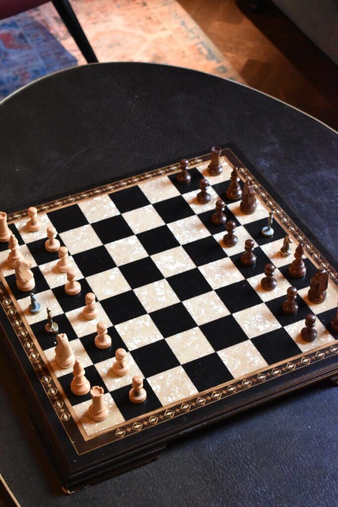 A chessboard with wooden pieces is set up in the middle of a game on a black table, with both black and white pieces visible.